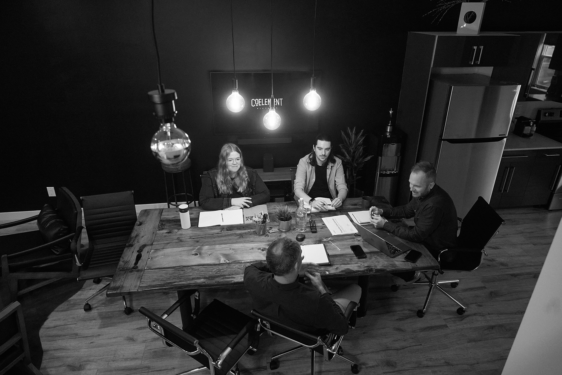 A black and white image of 5 Coelement team members working together at a wooden conference room table.