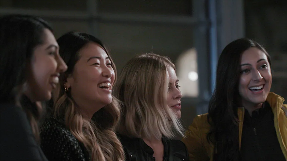 An image of a group of young women in the University of Manitoba Paediatrics Residency program smiling and laughing together in a dimly lit indoor space.