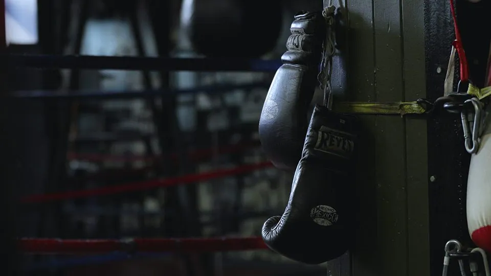 An image of boxing gloves hanging on a wooden pillar in a boxing arena.