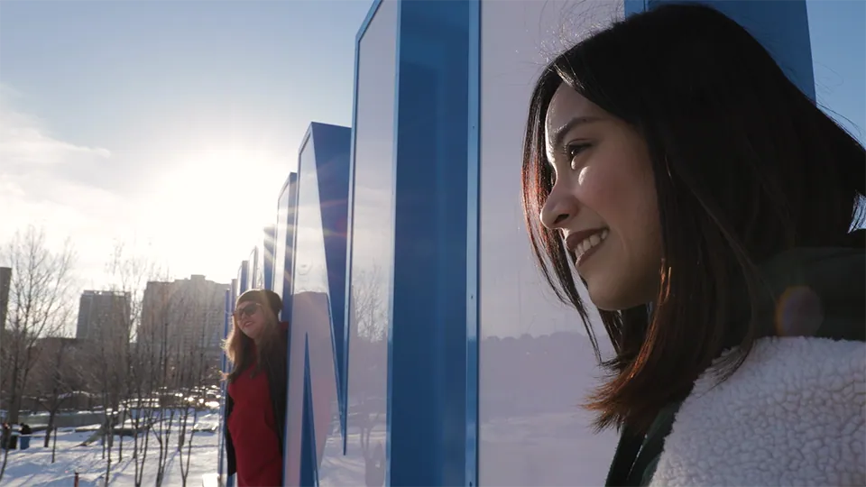 A profile image of a smiling woman standing beside the giant Winnipeg sign at the Forks in Winnipeg, Manitoba. The sun is shining and there is snow on the ground.