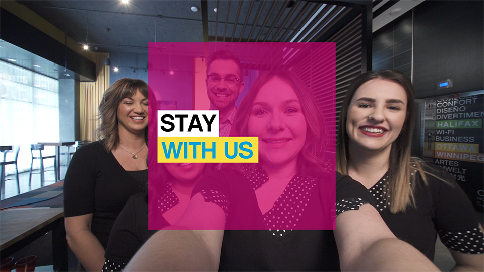 An image of a group of smiling women taking a photo together with the words "Stay With Us" overlaid over the group, on a transparent pink square.