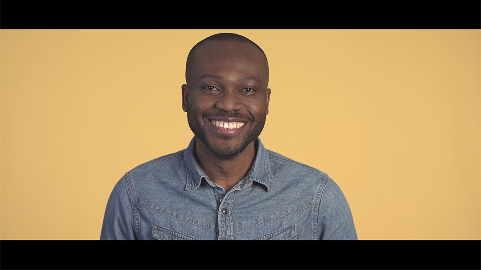 An image of a smiling man facing forward, against a yellow background.