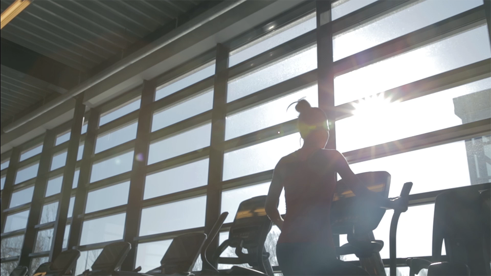 An image of a woman using an elliptical against a wall of windows with the sun shining through.