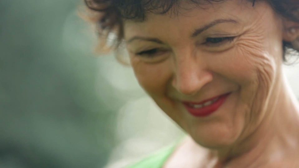 A close up profile image of an older woman smiling and looking down.