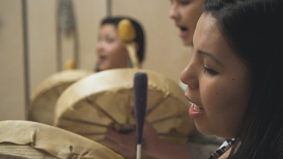 A close up profile image of a group of indigenous people chanting and playing drums.