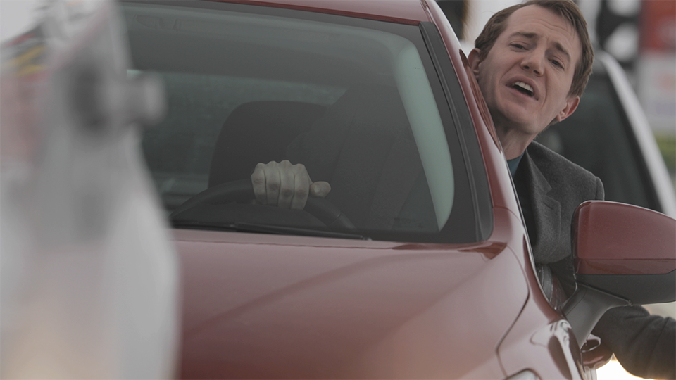 An image of a man sticking his head out of a car window and speaking.