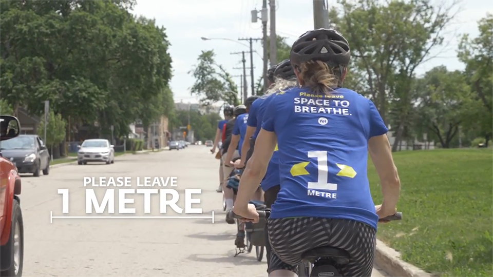 An image of a row of bikers biking down a residential street. A text graphic on the screen states "Please leave 1 meter."