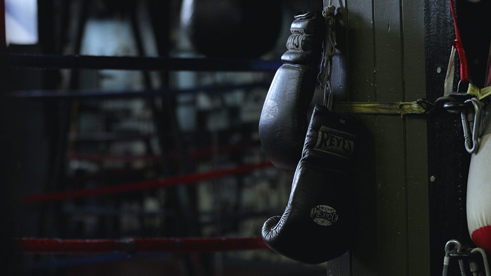 An image of boxing gloves hanging on a wooden pillar in a boxing arena.