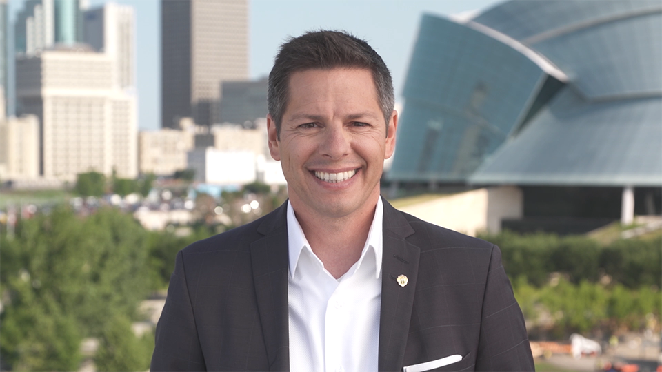 An image of Bryan Bowman smiling with The Canadian Museum for Human Rights and downtown Winnipeg in the background.