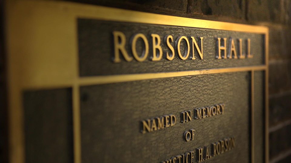 A closeup image of a gold engraved memorial sign for Robson Hall at the University of Manitoba.