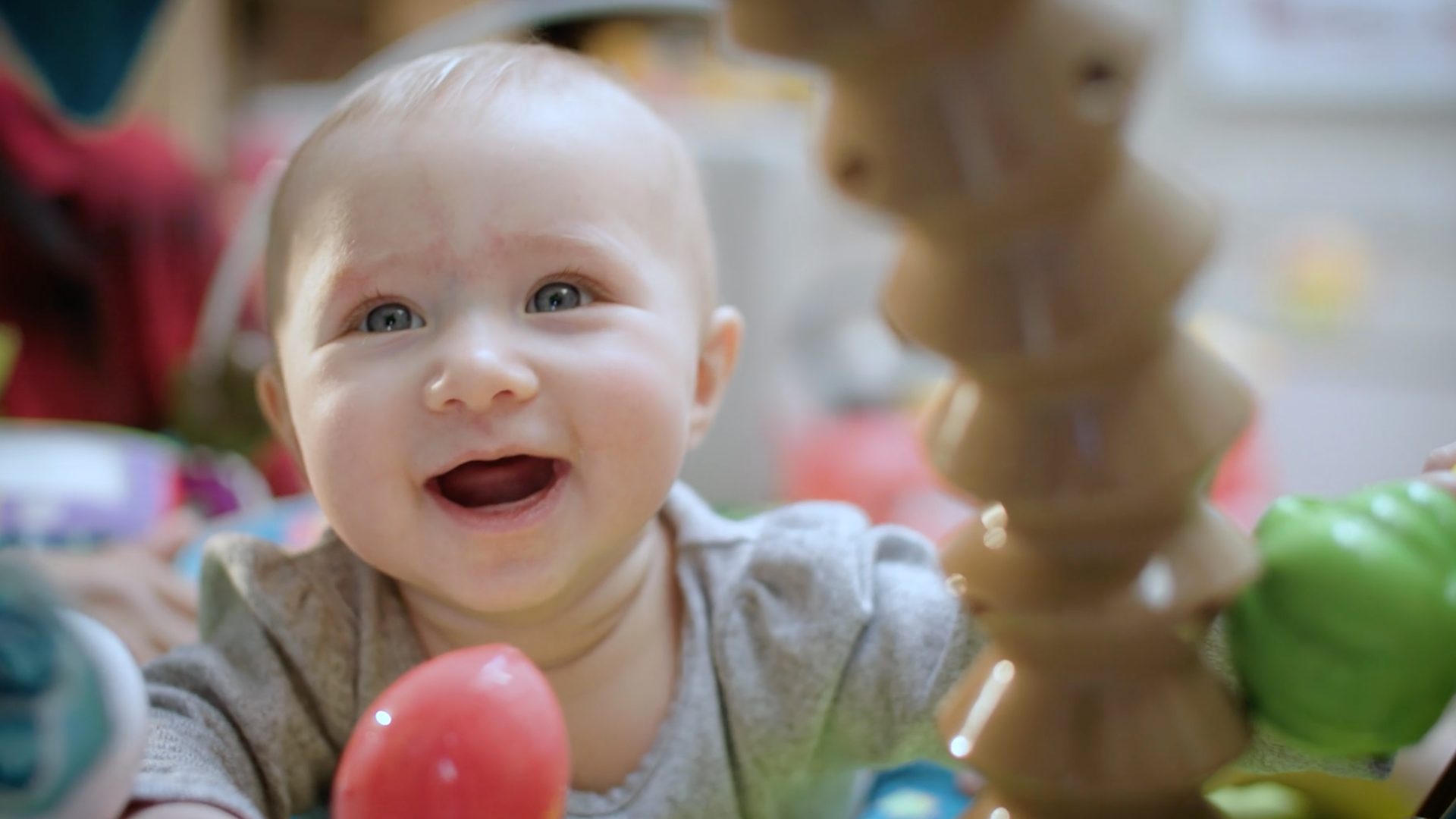 A style frame from a video for Ronald Mcdonald House, featuring a baby smiling, while looking up and lying on her stomach.