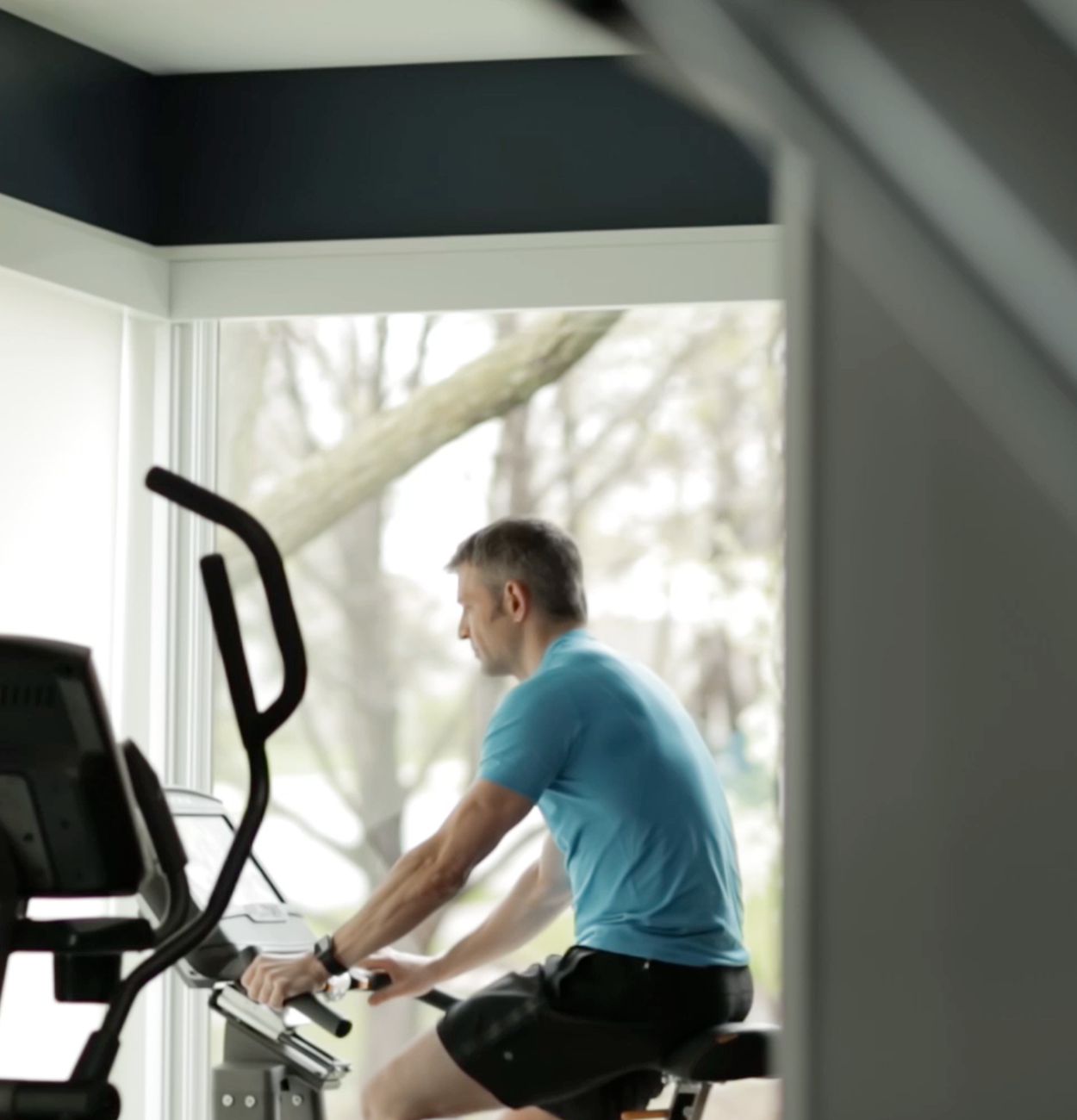 A middle aged man riding a stationery bike in front of a window.