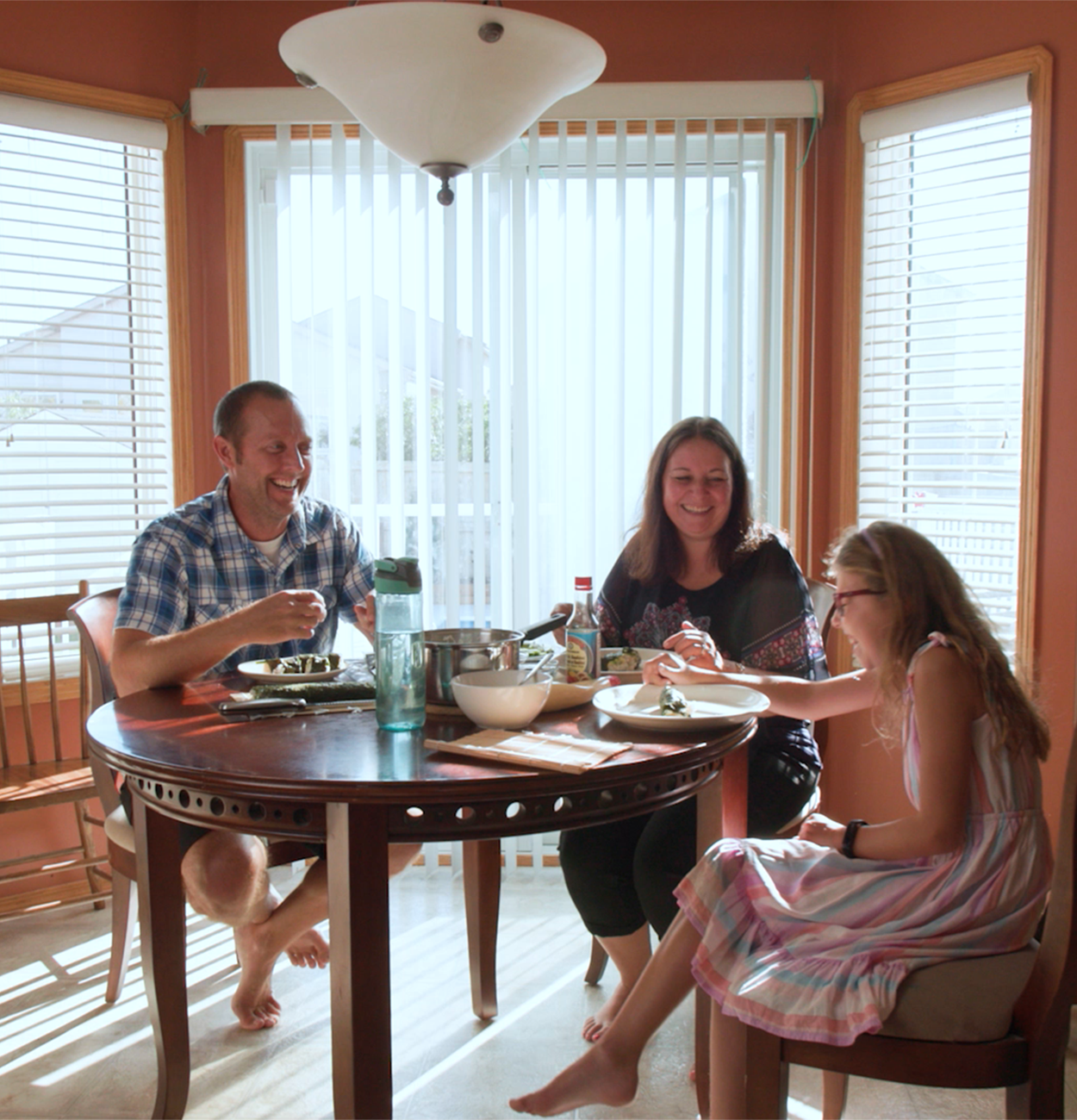 An image of a mother, father and daughter making sushi at a dining room table.